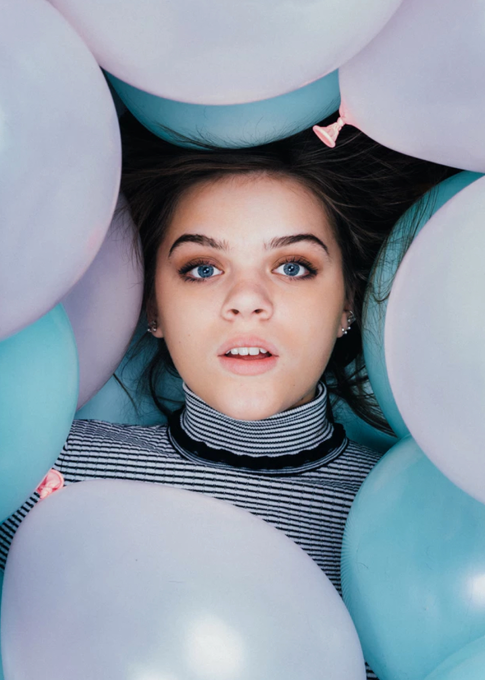 young girl lying among blue and pink ballons